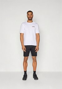 Balti trumpomis rankovėmis marškinėliai su raudonos ir juodos spalvų grafikos detalėmis, derinami su juodais šortais ir juodais sportbačiais. Paprastas, kasdienis dizainas.