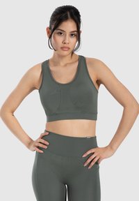 Sujetador deportivo de color verde oliva con un diseño ajustado, tirantes anchos y tela texturizada. Costuras en el busto y una banda elástica en el dobladillo.