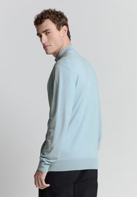 Lichtblauwe trui met lange mouwen en geribbelde zoom. Heeft een hoge kraag en een soepele textuur, tegen een neutrale achtergrond.