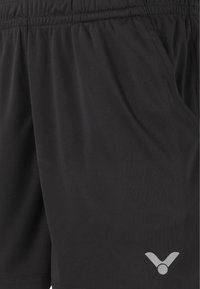 Sorte atletiske shorts lavet af letvægtsstof med en elastisk talje, sidelommer og en reflekterende logo detalje nederst på kanten.