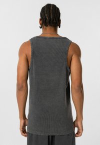 Grijze mouwloze katoenen tanktop met ribbelstructuur, ruwe zoom en ronde halslijn, gepresenteerd vanuit de achterkant.