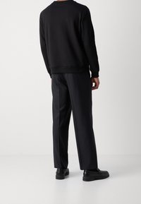 Sweat-shirt noir à encolure arrondie, associé à un pantalon noir. La tenue présente une coupe décontractée et une texture lisse. Des chaussures noires complètent le look.