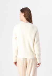 Maglione a maglia color crema con una texture morbida e pelosa, caratterizzato da un collo rotondo e vita e polsini a coste. Vista posteriore mostrata.