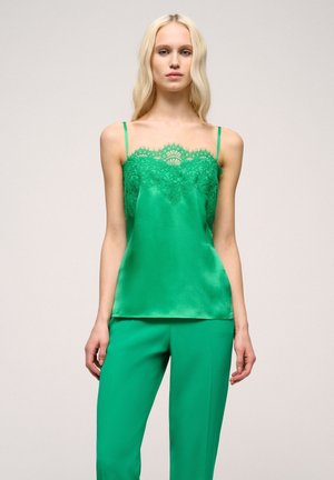 Camisă verde din satin cu dantelă, cu bretele subțiri și o croială lejeră. Asortată cu pantaloni verzi, creând o ținută coordonată.