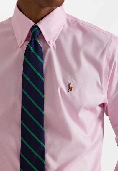 Heled roosa kaelusega särk nupudetailidega ja väikese tikitud hobuse logoga. Koos tumesinise lipsuga, millel on rohelised triibud.