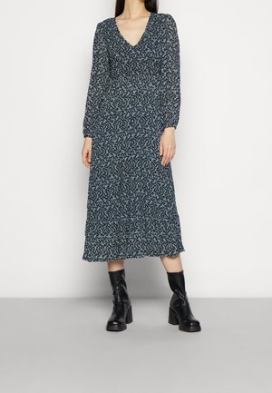 Robe à manches longues, à fleurs avec un décolleté en V, présentant une base bleu foncé et de petits motifs blancs et bleu clair. Ourlet froncé, accompagnée de bottes noires.