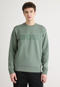 Felpa verde con colletto rotondo, caratterizzata da un logo "BOSS" in rilievo sul davanti. Realizzata in un tessuto morbido con una finitura testurizzata.