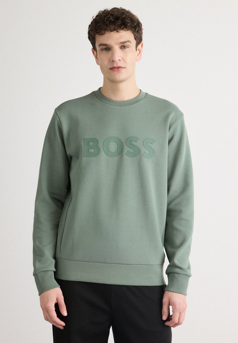 Felpa verde con colletto rotondo, caratterizzata da un logo "BOSS" in rilievo sul davanti. Realizzata in un tessuto morbido con una finitura testurizzata.
