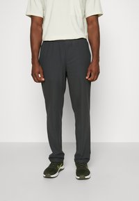 Graue Sporthose mit einer Kordelzugbundweite, schmal zulaufenden Beinen und leichtem Stoff. Kombiniert mit grünen Turnschuhen mit gelben Akzenten.