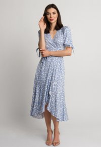 Niebieska sukienka na ramiączkach z białymi kwiatowymi wzorami, krótkie bufiaste rękawy i falbaniasty dół. Lekka tkanina, długość do kolan z dekoltem w kształcie litery V.