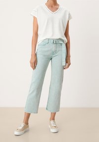 Top blanco de manga corta y cuello en V combinado con unos jeans de tiro alto en azul claro, que incluyen un cinturón y pierna ancha. Zapatillas beige completan el conjunto.