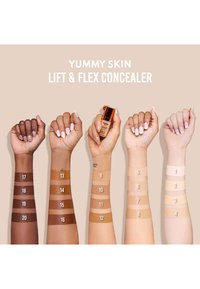 Fargeprøver av Yummy Skin Lift & Flex Concealer på forskjellige hudtoner, med nummererte striper i ulike nyanser fra dyp til lys.