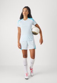 Svetlo modrý športový set Nike s krátkymi rukávmi, zodpovedajúce šortky a biele ponožky. Obsahuje okrúhly výstrih a čierno-zlatý futbalový loptu.