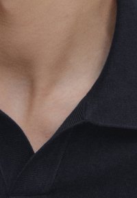 Musta poolopaidan kaulus, jossa resorikuvio, nähtynä kaulan alueelta. Kangas näyttää sileältä, siistillä ja jäsennellyllä muotoilulla.