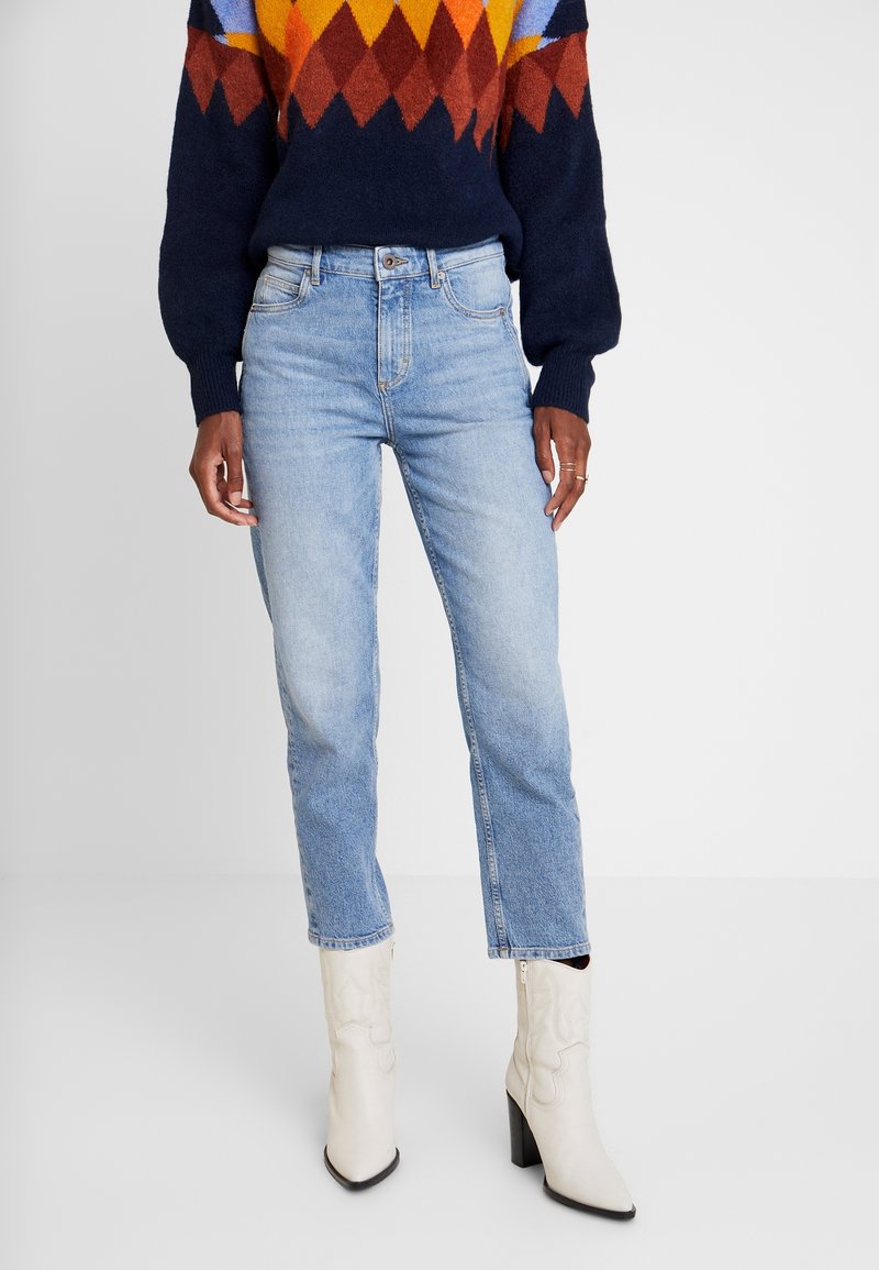 Jeans in denim azzurro chiaro con taglio dritto, indossati con un maglione a motivo multicolore e stivali bianchi con tacco alto.