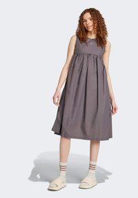 Grå ärmlös klänning med samlad midja och knä-lång fåll, gjord av lättviktsmaterial. Kombinerad med krämfärgade slip-ons och randiga strumpor.