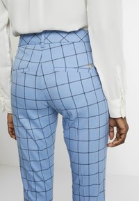 Light blue checkered trousers with a smooth texture, featuring a slim fit, back pockets, and a decorative button detail.