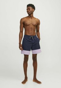 Costumi da bagno blu navy con orlo lilla, realizzati in tessuto leggero, dotati di tasche laterali e cintura elasticizzata con cordino.
