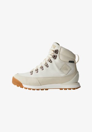 Botte de randonnée blanche avec tige en suède et tissu, œillets en métal et semelle en caoutchouc proéminente. Présente des accents de marque et une finition texturée.