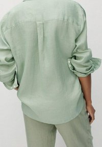 Lichtgroen linnen overhemd met opgerolde mouwen, naad in het achterpand en knoopmanchetten. Zachte textuur, losse pasvorm en casual ontwerp.