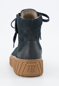 Bottine en cuir bleu marine foncé avec une tige texturée et une semelle en caoutchouc tan contrastante arborant un motif géométrique et un détail de logo au niveau du talon.