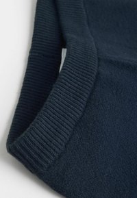 Gros plan sur le col d'un pull en maille bleu marine foncé avec une texture côtelée sur le tour du cou et un corps en laine douce.