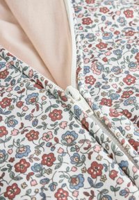 Vaate zip-up kukkakuosisella kankaalla, jossa valkoinen pohja ja monivärisiä kukkia vaaleanpunaisena, punaisena, sinisenä ja vihreänä. Pehmeä rakenne, jossa on erottuva sisävuori.