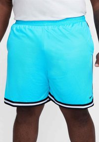 Άνδρας που φορά φωτεινές μπλε αθλητικές βερμούδες με μαύρες και λευκές λεπτομέρειες και έναν μικρό λογότυπο Nike στο αριστερό πόδι, στέκεται με τα χέρια στο πλάι.