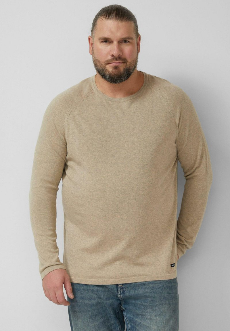 Beżowa koszulka z długim rękawem i okrągłym dekoltem, wykonana z miękkiego materiału, o luźnym kroju i subtelnej fakturze. Połączona z niebieskimi jeansami.