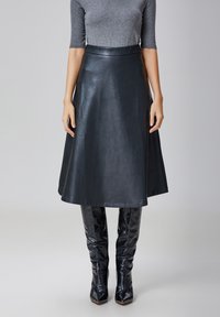 Jupe en cuir noir en A avec une taille haute, atteignant le mollet, associée à des bottes noires brillantes hautes jusqu'au genou. Texture lisse, design minimaliste.