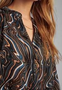 Blusa nera con un motivo astratto ondulato in blu, arancione e bianco. Presenta un collo a V e delle delicate pieghe sulle spalle.