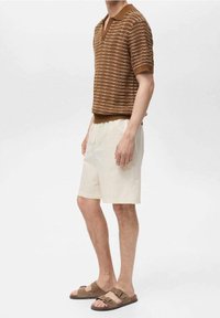 Hnědý pruhovaný polo tričko s krátkým rukávem a hlubokým V-výstřihem, s žebrovaným lemem, v kombinaci s krémovými šortkami a hnědými sandály se dvěma sponami.