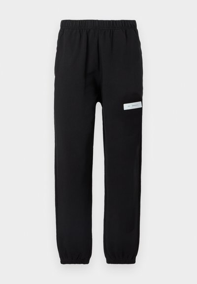 Μαύρο παντελόνι φόρμας με ελαστική μέση, στενά μπατζάκια και λευκή ετικέτα στην αριστερή πλευρά. Ομαλή υφή, casual σχεδίαση.