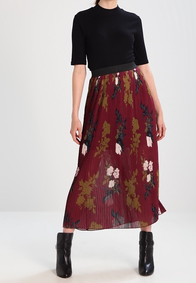 Haut noir à manches courtes associé à une jupe longue plissée bordeaux ornée de motifs floraux roses et verts. Bottines en cuir noir.