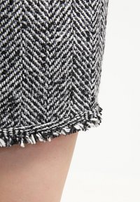 Tissu à motif chevron noir et blanc avec un ourlet effiloché, mettant en valeur un tissage texturé et une légère brillance. Gros plan sur le détail du short.