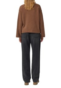 Brauner Strickpullover mit überschnittenen Schultern, kombiniert mit locker sitzenden dunkelgrauen Jeans mit hoher Taille und klassischem Fünf-Taschen-Design.