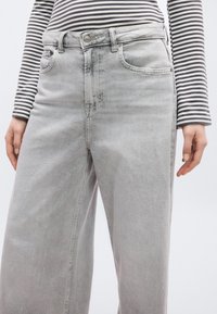 Γκρι τζιν παντελόνι με ευρύ πόδι διαθέτει κλασικό σχεδιασμό με πέντε τσέπες και κουμπωτή ντούλαπα. Το ύφασμα έχει απαλή, ελαφρώς υφασμένη υφή.