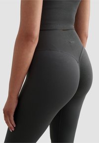 Legginsy w ciemnoszarym kolorze z wysokim stanem, o prążkowanej teksturze i gładkim wykończeniu. Posiadają subtelne logo z tyłu oraz dopasowany krój.