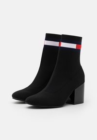 Bottines noires de style chaussette avec un talon épais noir. Présentent un design de poignet rayé rouge, blanc et bleu près du haut. Texture lisse.