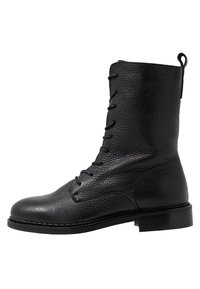 Czarne skórzane buty za kostkę na sznurówki o fakturowanym wykończeniu, z zaokrąglonym czubkiem, wzmocnionym piętem i płaską podeszwą. Posiadają pętelkę do zakupu na górze.