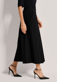 Zwarte, vloeiende rok met een hoge taille en plooien. Gecombineerd met zwarte, puntige hakken met een enkelbandje. Gladde textuur.