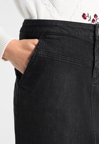 Falda de mezclilla negra con una silueta ajustada. Cuenta con un bolsillo lateral, detalles de costura sutil y una textura suave.