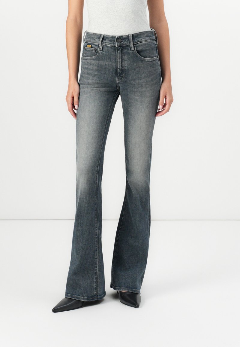 Jeans bootcut in denim grigio sbiadito, con un classico design a cinque tasche e una leggera svasatura all'orlo, abbinati a scarpe nere a punta.