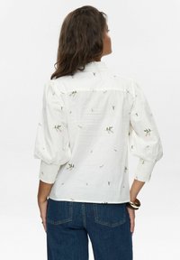 Blusa bianca con ricami floreali, maniche a sbuffo e polsini arricciati. Tessuto leggero, vestibilità ampia e colletto.