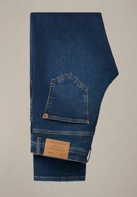 Jeans denim w ciemnoniebieskim kolorze, z charakterystyczną, kwadratową tylnią kieszenią, mosiężnymi detalami oraz brązową metką na pasie.