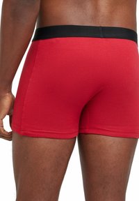 Boxers rouges en coton avec une ceinture élastique noire, présentant une texture douce et un ajustement serré autour des cuisses.