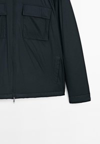 Black insulated jacket with a zip front, featuring two chest pockets, side pocket, and a slightly puffy texture. Simple, functional design.