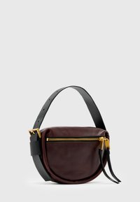 Brun lær crossover-veske med en buet form, svart rem og gullglidelås. Bemerkelsesverdige detaljer inkluderer frynser og strukturerte hardware-accents.