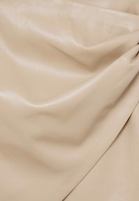 Beige leren stof met een gladde, glanzende textuur en zachte val, met voorzichtig overlappende plooien en een subtiele glans over het oppervlak.