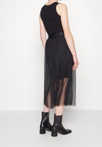 Mustat kerrokselliset tüllihameet, joissa on istuva vyötärö, jossa on DKNY-logo. Yhdistetty tyylikkäisiin mustiin nilkkabootseihin.
